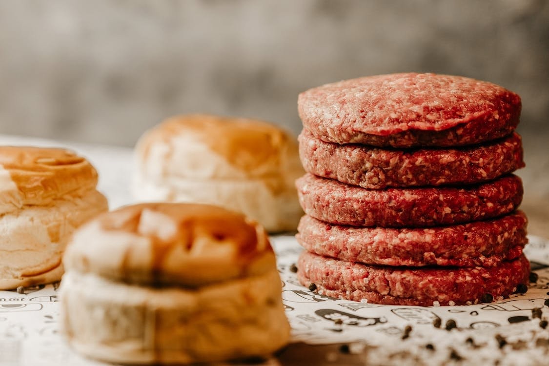 Raw burger patties stacked with brioche buns