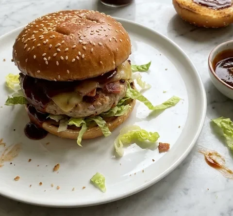 Gordon Ramsay pork burger with smoky bacon patty, melted applewood Cheddar, barbecue sauce and shredded lettuce on a sesame bun