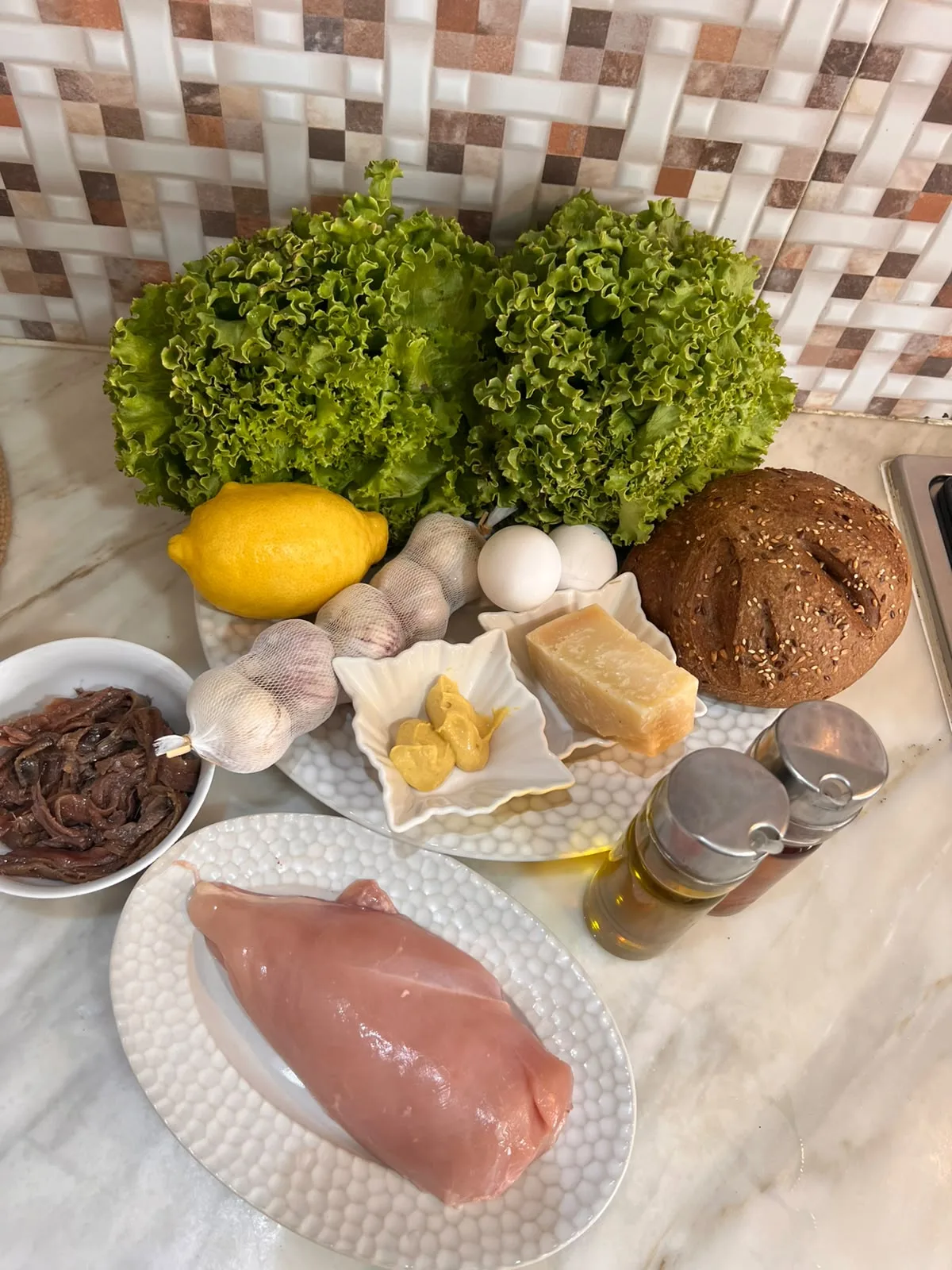 Ingredients for Gordon Ramsay caesar salad: batavia lettuce, lemon, garlic, eggs, Parmesan, seeded bread loaf, Dijon mustard, anchovies, chicken breast and olive oil