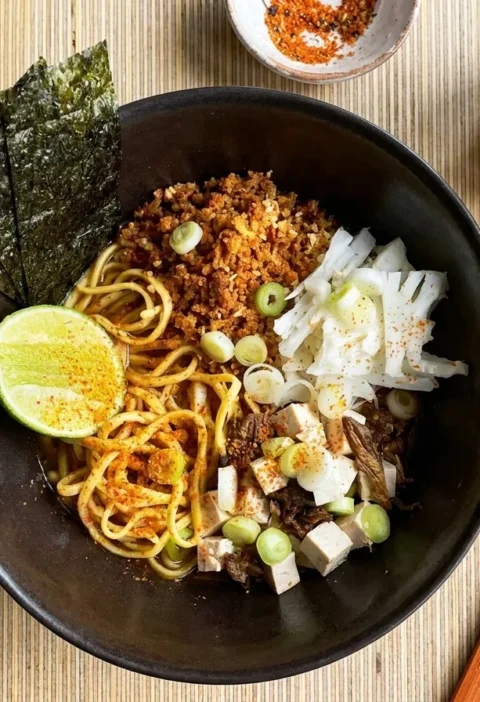 Gordon Ramsay cauliflower ramen with crispy fried cauliflower, tofu, egg noodles, nori and shichimi lime in a dark bowl